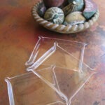 Clear, decorative trays are positioned on a rustic table next to a bowl of colorful, decorative fruits, enhancing the table's aesthetic appeal.