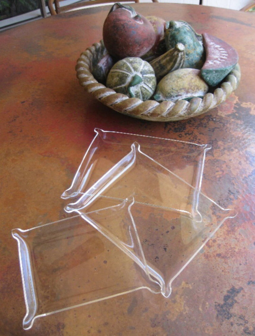 Clear, decorative trays are positioned on a rustic table next to a bowl of colorful, decorative fruits, enhancing the table's aesthetic appeal.